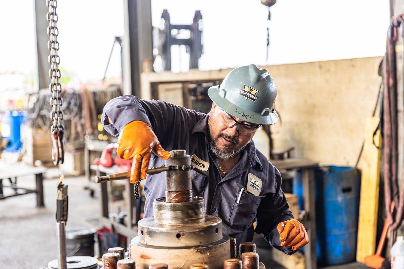 A Supreme technician guiding a frac valve body into place in the Corpus Christi yard.
