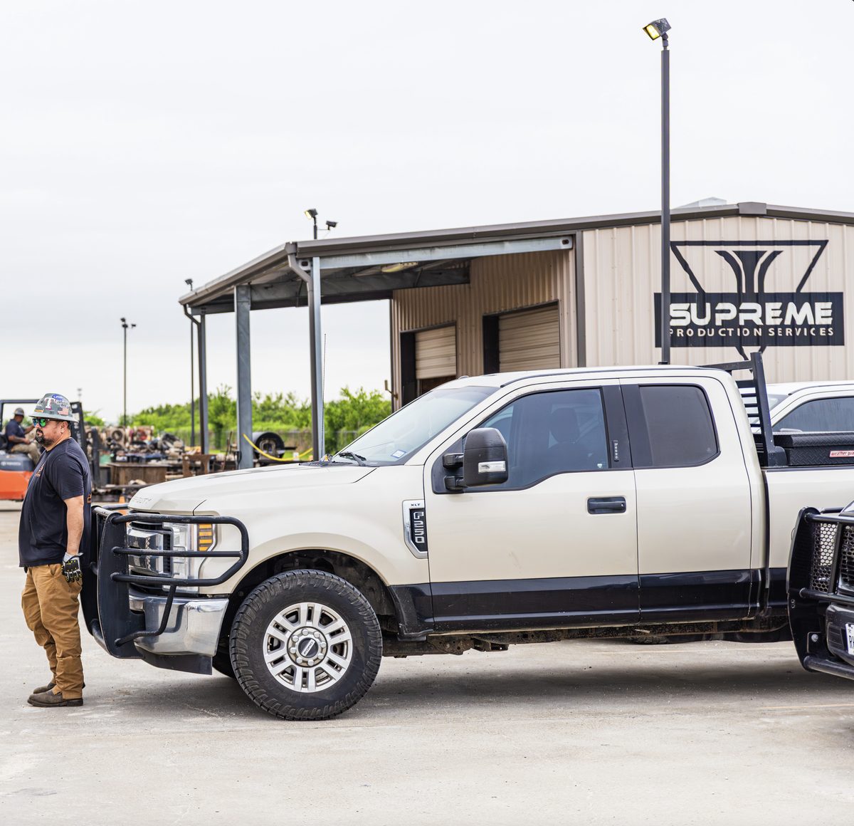 A Supreme Production Services crew member beside a company truck in the yard at the Corpus Christi headquarters, with the shop building behind.